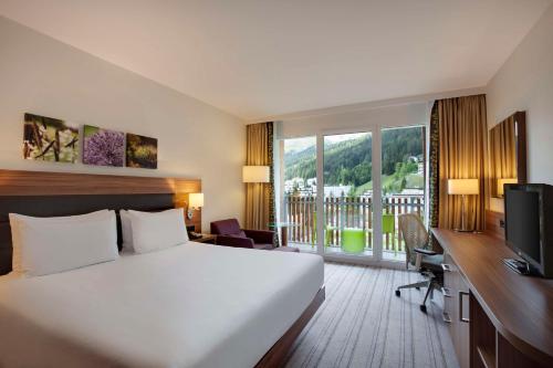 Habitación de hotel con cama y escritorio con TV. en Hilton Garden Inn Davos en Davos