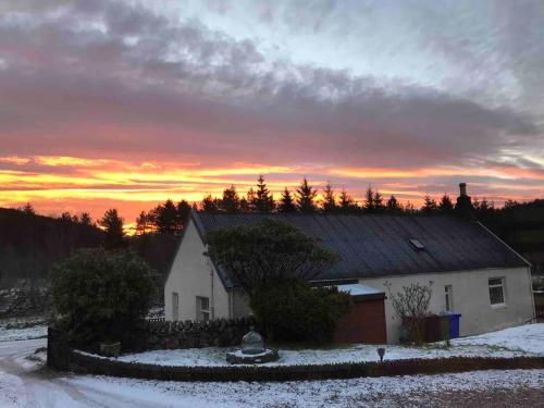 a house in the snow with a sunset in the background at Cosy Highland Cottage Tyndrum centrally located in Tyndrum