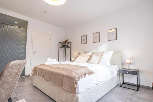 a white bedroom with a bed and a chair at Krems Bahnhof Deluxe Rooms - near Danube River in Krems an der Donau