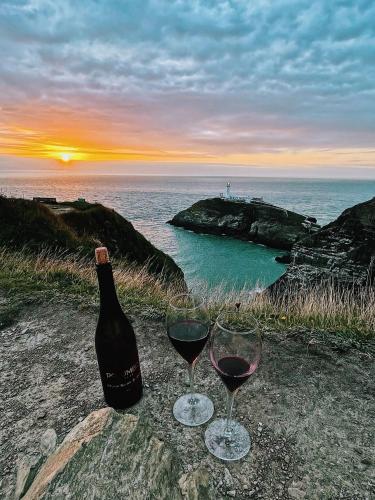two glasses of wine sitting on a rock with the ocean at Goferydd, South Stack, Anglesey, 4 bed luxury home, hot tub, dog friendly in Holyhead
