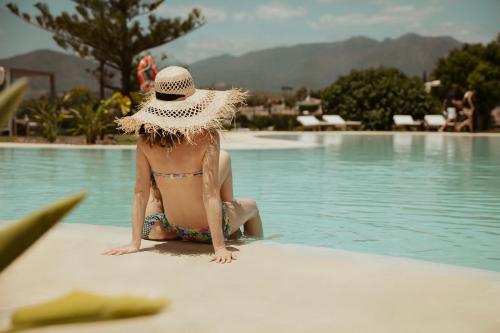 una mujer con sombrero sentada junto a una piscina en La Zambra Resort GL, part of The Unbound Collection by Hyatt en Mijas