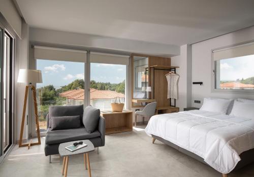 a bedroom with a bed and a chair and a window at Nikiti Botanic Pool Suites in Nikiti