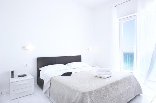 a white bedroom with a bed and a window at Vuelle Residence Apartments in Capo dʼOrlando