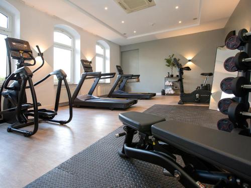 a gym with several treadmills and exercise bikes at DORMERO Hotel Worms in Worms