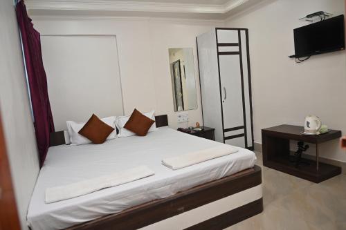 Schlafzimmer mit einem Bett mit weißer Bettwäsche und einem TV in der Unterkunft HOTEL GITANJALI in Māldah