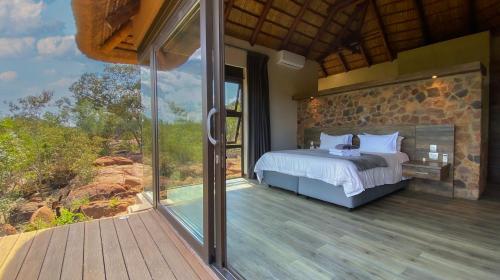 a bedroom with a bed and a large glass window at Shammah lodge Mabalingwe Nature Reserve in Mabula