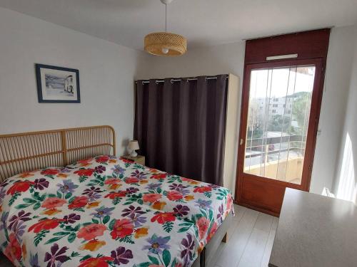 1 Schlafzimmer mit einem Bett mit Blumenbettdecke und einem Fenster in der Unterkunft T2 climatisé 3* avec Loggia, Parking sécurisé, WiFi, proche plage - Bormes-les-Mimosas - FR-1-610-98 in Bormes-les-Mimosas