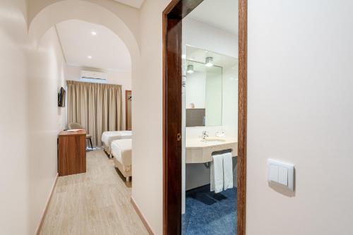 Catolica Hotel في فاطمة: حمام فيه سرير ومغسلة ومرآة