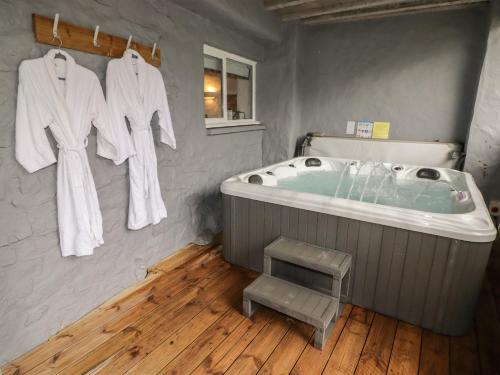 a bathroom with a tub with white robes hanging on a wall at Le Durkestrete Cellar in Haverfordwest