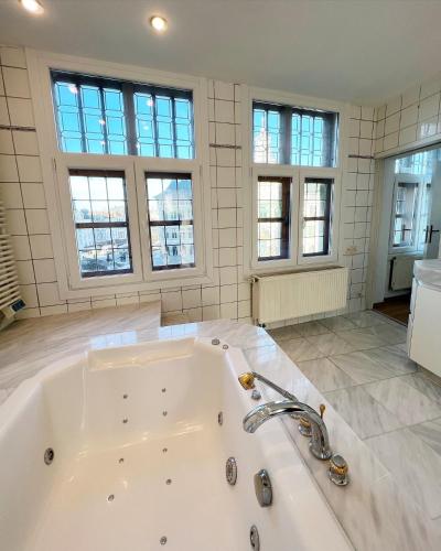 a large white bath tub in a room with windows at Le FauBourg Suites in Antwerp