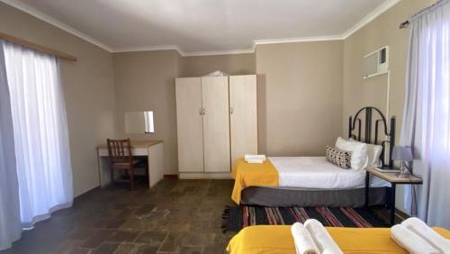 1 Schlafzimmer mit 2 Betten und einem Schreibtisch mit einem Tisch in der Unterkunft Stoney's Country Hotel in Gochas