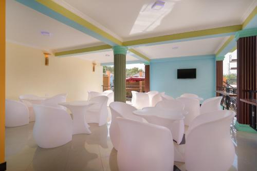 Habitación con sillas blancas y TV de pantalla plana. en New Mazubu Grand Hotel Mererani en Mbuguni