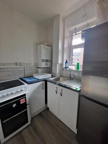 a kitchen with white cabinets and a sink and a refrigerator at Comfortable 2 bedrooms flat in Oval Central London in London