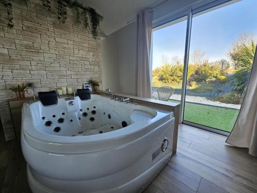 a large white tub in a bathroom with a large window at L'Essentiel - Love 85 in Talmont