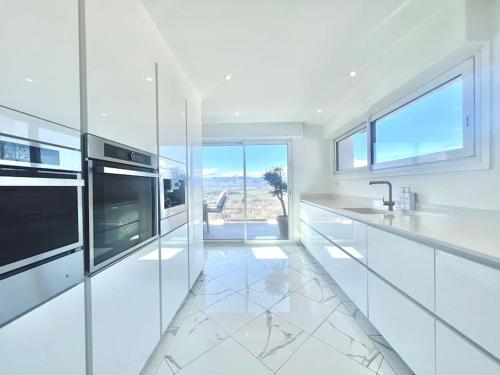 une cuisine blanche avec des appareils électroménagers blancs et une grande fenêtre dans l'établissement Villa contemporaine d'architecte, à Bonneville