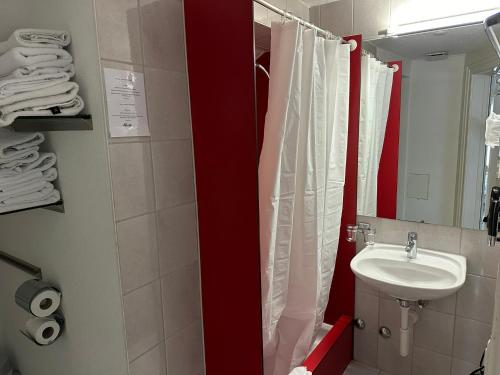 a bathroom with a white sink and a red shower curtain at Hotel Spatz in Luzern