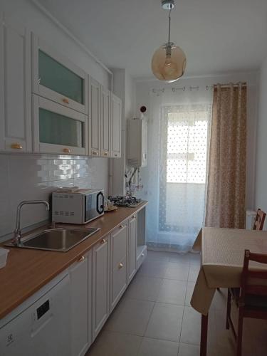 a kitchen with white cabinets and a sink and a window at Safirului apartment in Bragadiru