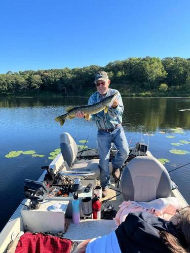 a man standing on a boat holding a fish at Escape to Nature and Lake views Studio Style Rooms in Clitherall