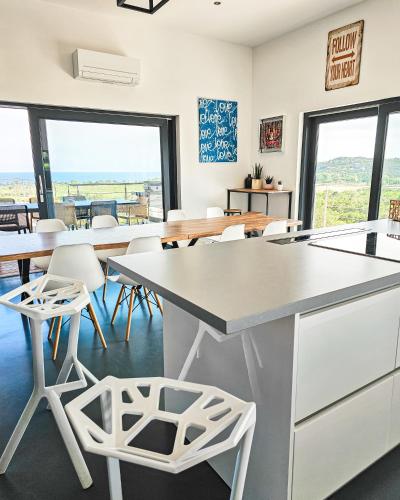 une cuisine avec des chaises blanches, des tables et des fenêtres dans l'établissement Villa Lavu Santu piscine privée vue mer/montagnes, à Zonza