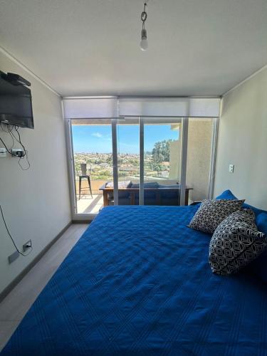 um quarto com uma cama azul e uma grande janela em EL PORTAL DE ALGORRO, V REGION,VALPARAISO em Algarrobo