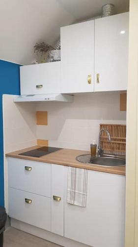 une petite cuisine avec des armoires blanches et un évier dans l'établissement F3 avec salle de jeux, terrasse et grand jardin, à Villevaudé