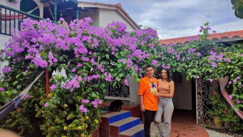a man and woman standing in front of a house with purple flowers at Casa Paula santa marta in Gaira