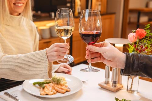 two people holding glasses of wine at a table with a plate of food at Hotel Krone in Mondsee