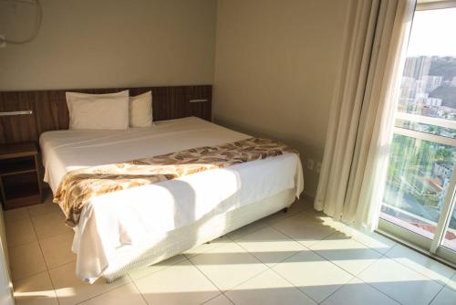 a bed in a room with a large window at Manhattan Apart Hotel in Caratinga