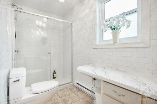 a white bathroom with a toilet and a window at Inn By The Park Morrisburg in Morrisburg