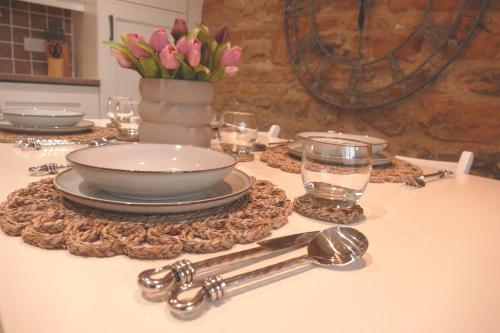 a table with plates and glasses and a vase of flowers at Immaculate 1-Bed Cottage in Moreton in marsh in Moreton in Marsh