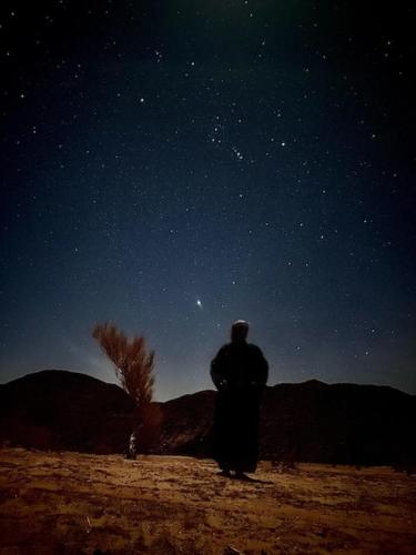 a man standing in the desert looking up at the night sky at وادي رم in Aqaba