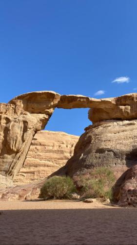 un arco en una pared de roca junto a un cuerpo de agua en وادي رم, en Áqaba