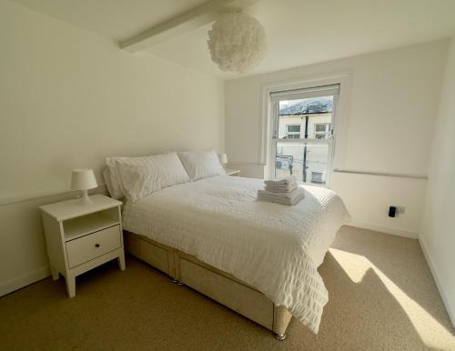 a white bedroom with a bed and a window at Buttercup Cottage in St. Leonards