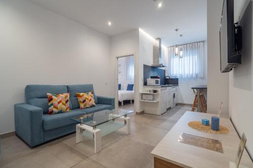 a living room with a blue couch and a kitchen at CMDreams Gold- Apartamentos turísticos con ruinas romanas en el centro de Mérida in Merida