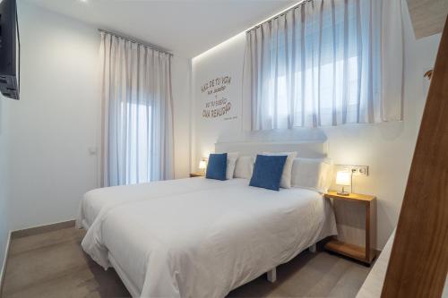 a bedroom with a large white bed with blue pillows at CMDreams Gold- Apartamentos turísticos con ruinas romanas en el centro de Mérida in Mérida