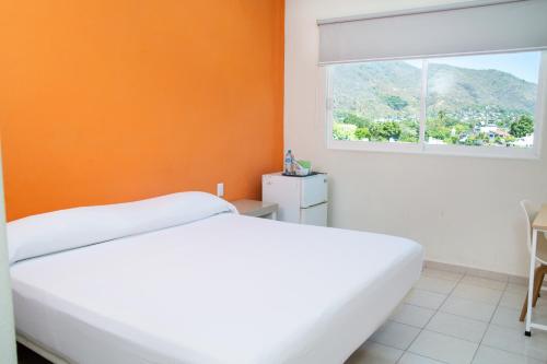 - une chambre avec un lit blanc et un mur orange dans l'établissement Fabuloso Hotel Las Vegas, à Zihuatanejo