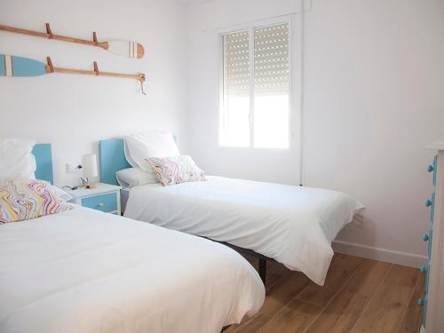 two beds in a white room with a window at Sanlucarsun Apartamento frente al mar in Sanlúcar de Barrameda