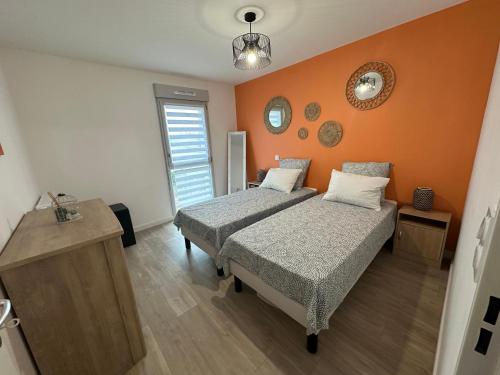 une chambre avec deux lits et un mur orange dans l'établissement L'émeraude, à Cancale