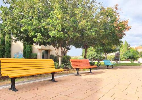 three benches in a park with trees in the background at Spacious and Peaceful 2BD with a Garden & Parking in Gan H̱ayyim