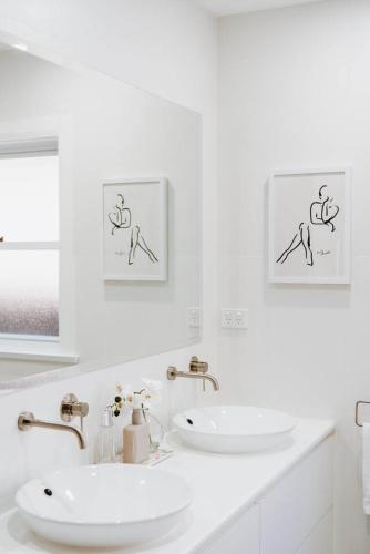 a white bathroom with two sinks and two pictures on the wall at 'Haylock' Luxe Country Charm in Mudgee's Centre in Mudgee
