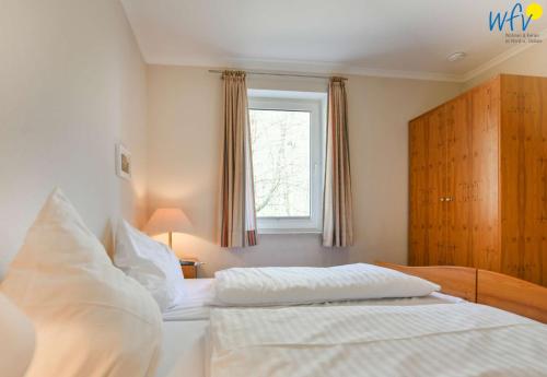 a bedroom with a bed with white sheets and a window at Haus am Hövt - Ferienwohnung 11 in Göhren
