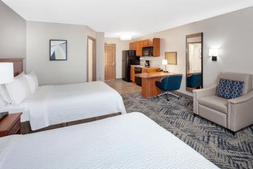 Habitación de hotel con 2 camas, silla y escritorio. en Candlewood Suites Louisville North, an IHG Hotel en Clarksville