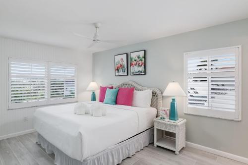 a white bedroom with a large white bed with colorful pillows at Breakers West C2 - Gorgeous Top Floor Beach Condo in Sanibel