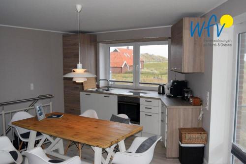 uma cozinha com uma mesa de madeira e cadeiras brancas em Haus Kiek in't Watt Ferienwohnung Deichrausch em Juist