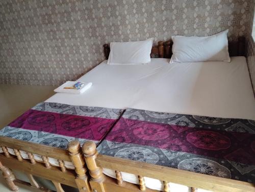 a bed with a wooden frame with a white bedsheet and flowers at D'Souza Rooms in Māvalli