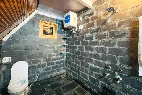 a bathroom with a stone wall and a toilet at Ashapuri Cottage near Rupi Raila Waterfall in Sainj