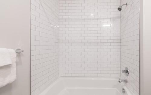 a white tiled shower with a white bath tub at Cozysuites l Gorgeous 1BR in Downtown Cincinnati in Cincinnati