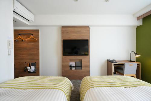 two beds in a room with a tv on a wall at Airport Hotel Kumamoto in Ozu