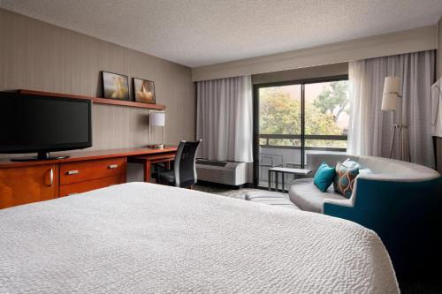 a hotel room with a bed and a desk and a television at Courtyard by Marriott San Francisco Airport in San Bruno
