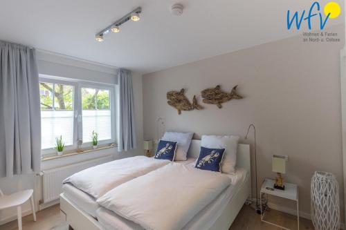 a bedroom with a white bed with blue pillows and a window at Juist Zauber - Haus 3 Ferienwohnung Strandaster in Juist